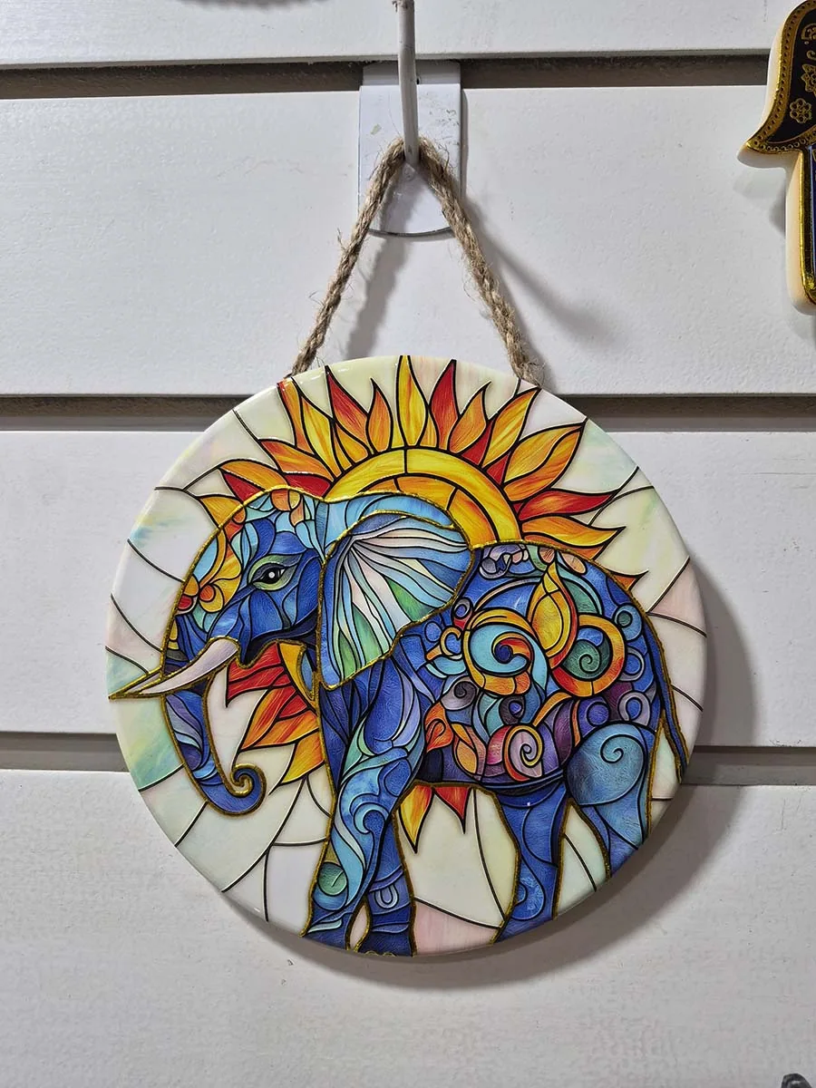 Colgante decorativo de pared de cerámica con un elefante frente a un sol naciente en tonos dorados y anaranjados