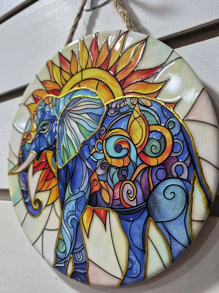 Colgante decorativo de pared de cerámica con un elefante frente a un sol naciente en tonos dorados y anaranjados