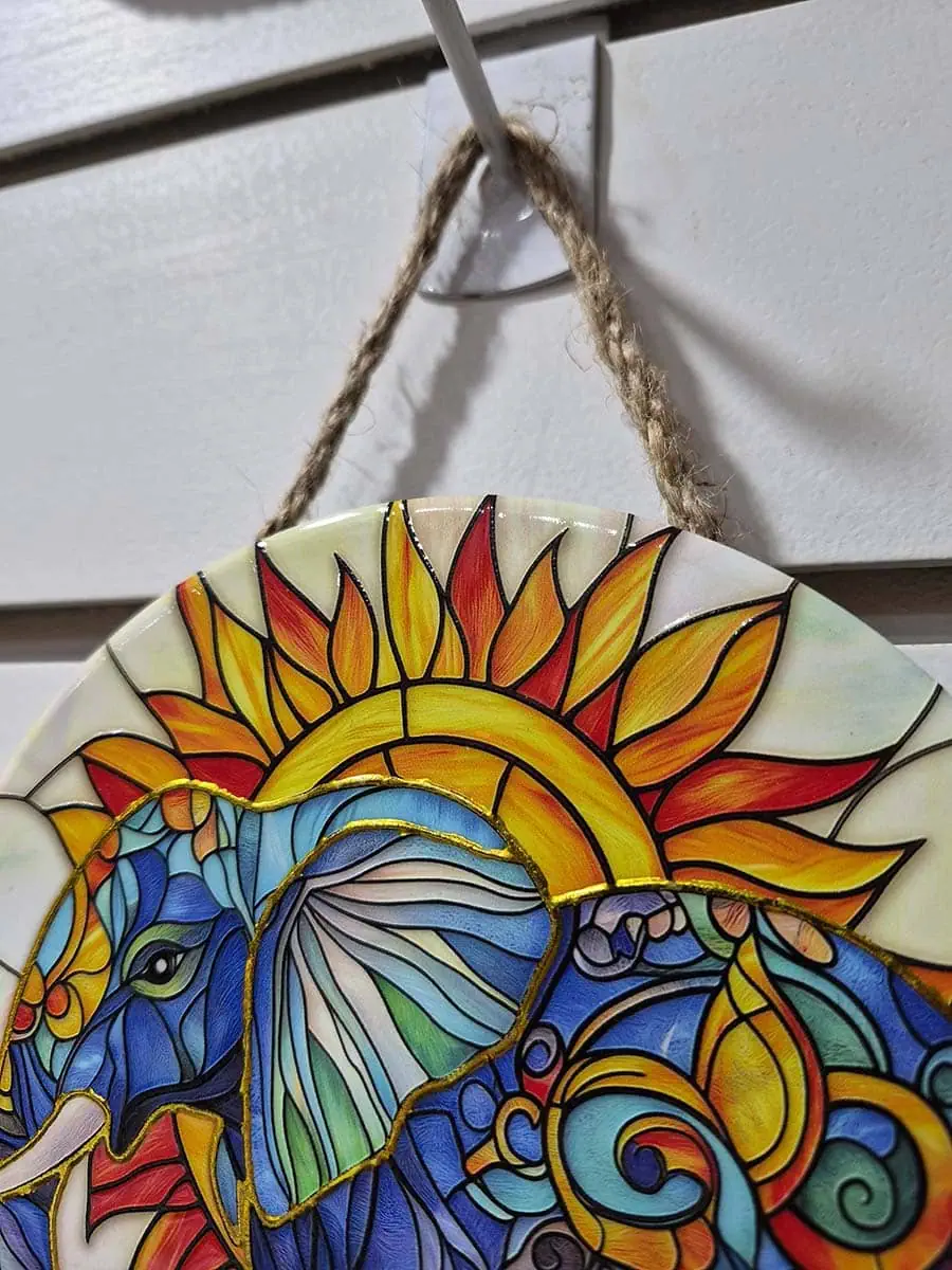 Colgante decorativo de pared de cerámica con un elefante frente a un sol naciente en tonos dorados y anaranjados