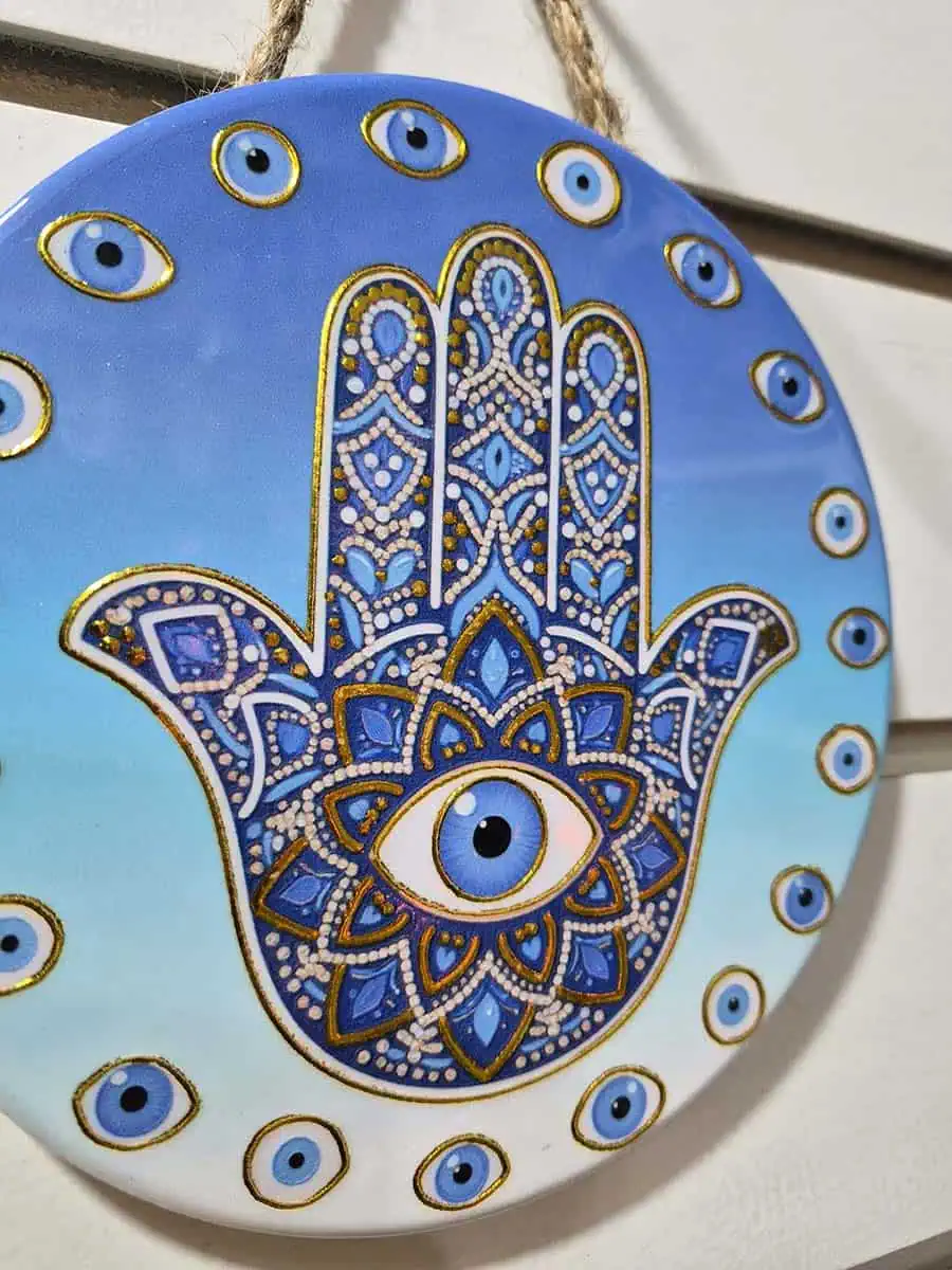 Colgante decorativo redondo de cerámica con Mano de Fátima y ojos turcos sobre fondo celeste