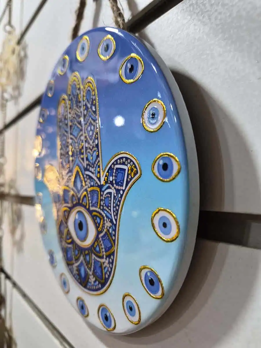 Colgante decorativo redondo de cerámica con Mano de Fátima y ojos turcos sobre fondo celeste