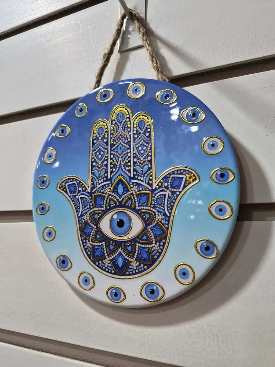 Colgante decorativo redondo de cerámica con Mano de Fátima y ojos turcos sobre fondo celeste