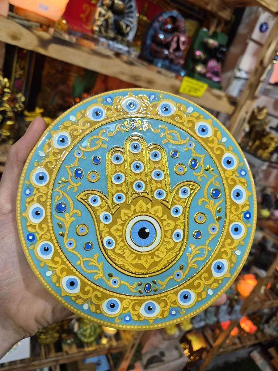Colgante decorativo redondo de cerámica con Mano de Fátima dorada y ojos turcos sobre fondo celeste agua