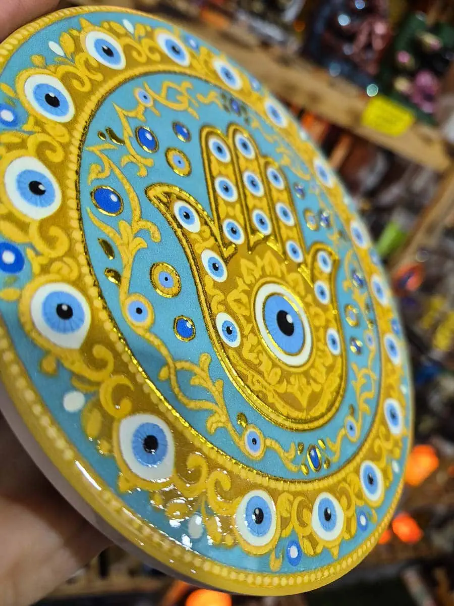 Colgante decorativo redondo de cerámica con Mano de Fátima dorada y ojos turcos sobre fondo celeste agua