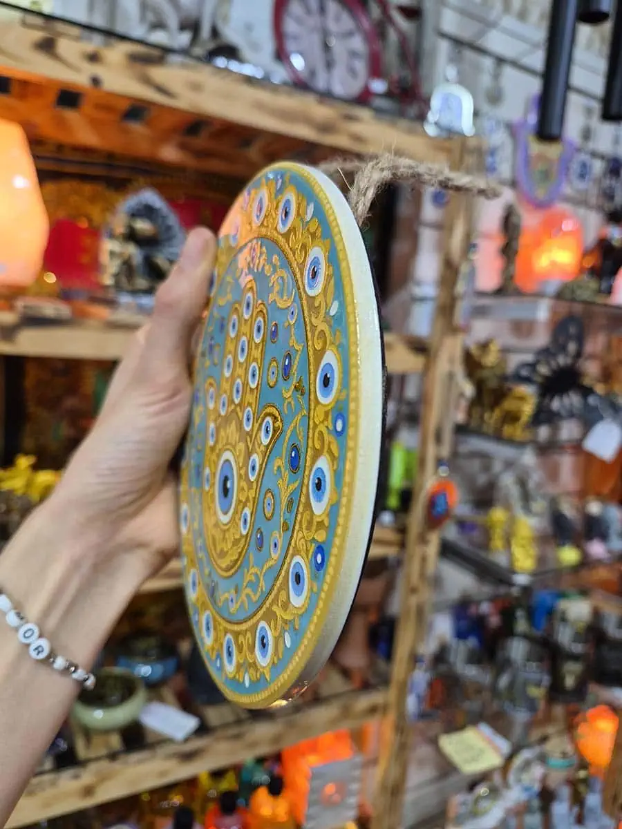 Colgante decorativo redondo de cerámica con Mano de Fátima dorada y ojos turcos sobre fondo celeste agua