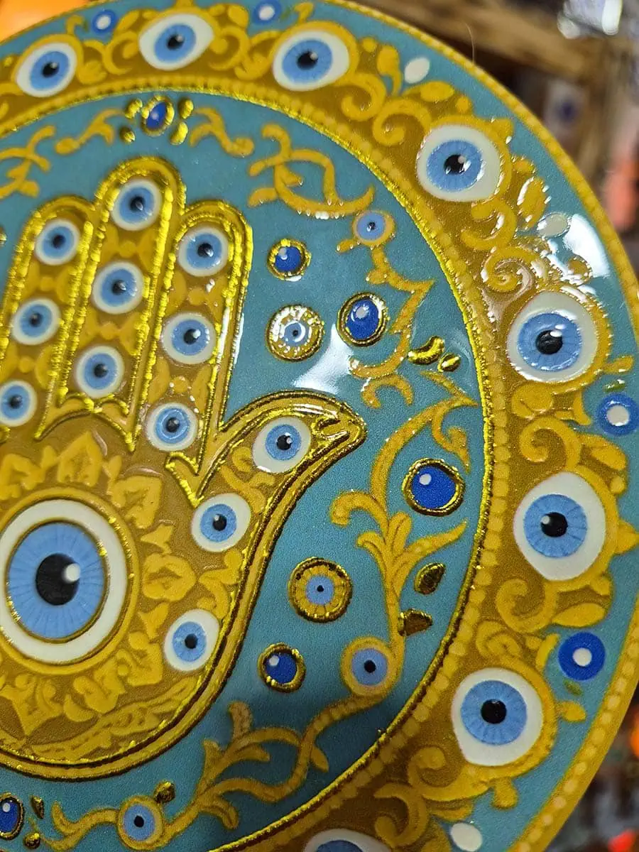 Colgante decorativo redondo de cerámica con Mano de Fátima dorada y ojos turcos sobre fondo celeste agua
