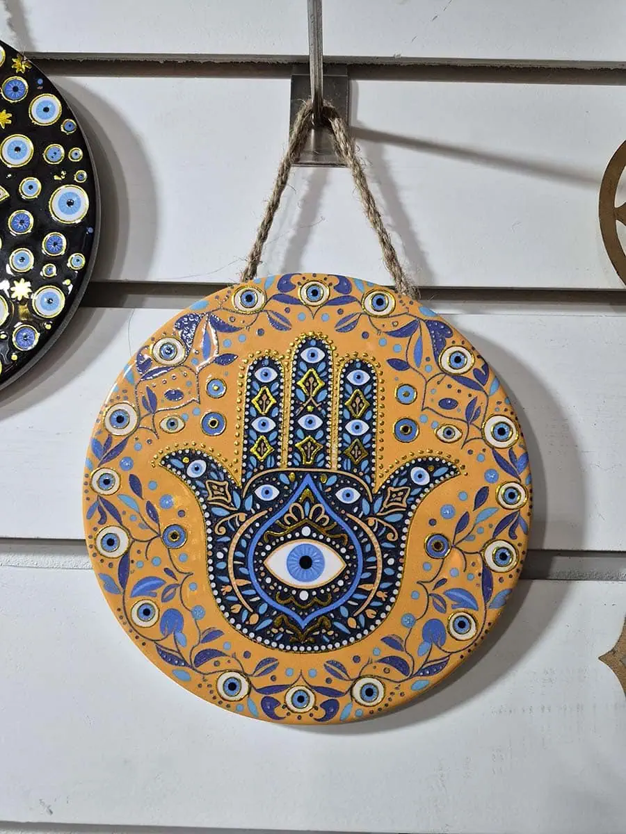 Colgante decorativo redondo de cerámica con Mano de Fátima azul, ojo turco y detalles florales sobre fondo naranja
