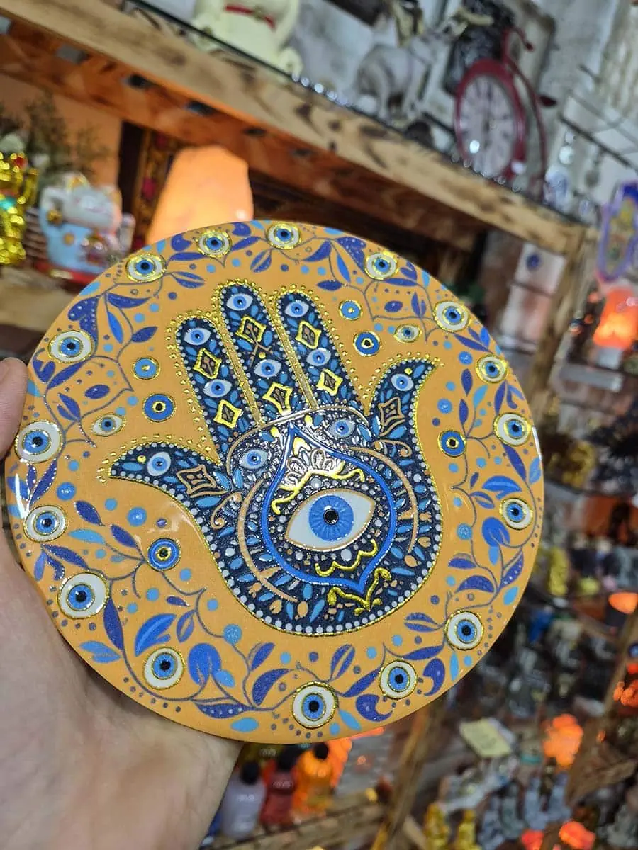 Colgante decorativo redondo de cerámica con Mano de Fátima azul, ojo turco y detalles florales sobre fondo naranja