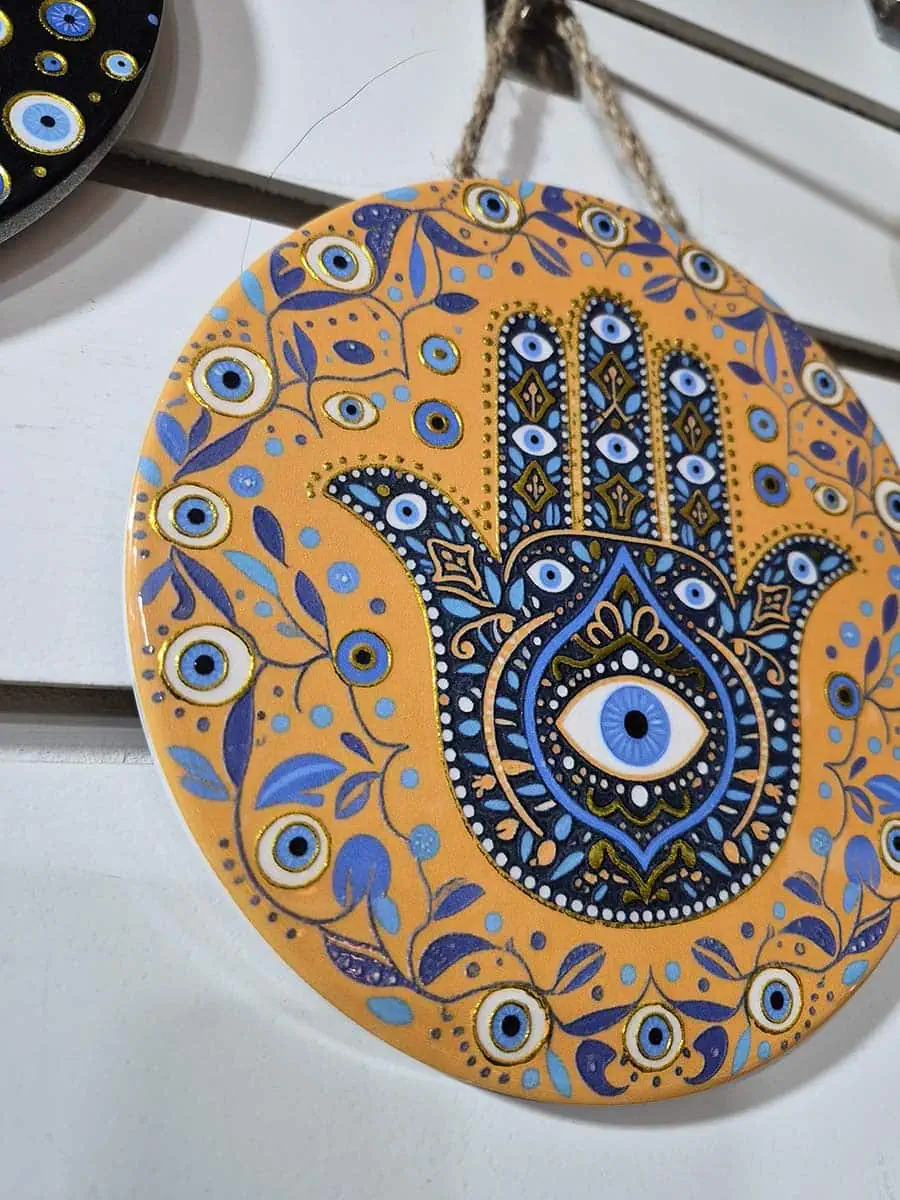 Colgante decorativo redondo de cerámica con Mano de Fátima azul, ojo turco y detalles florales sobre fondo naranja