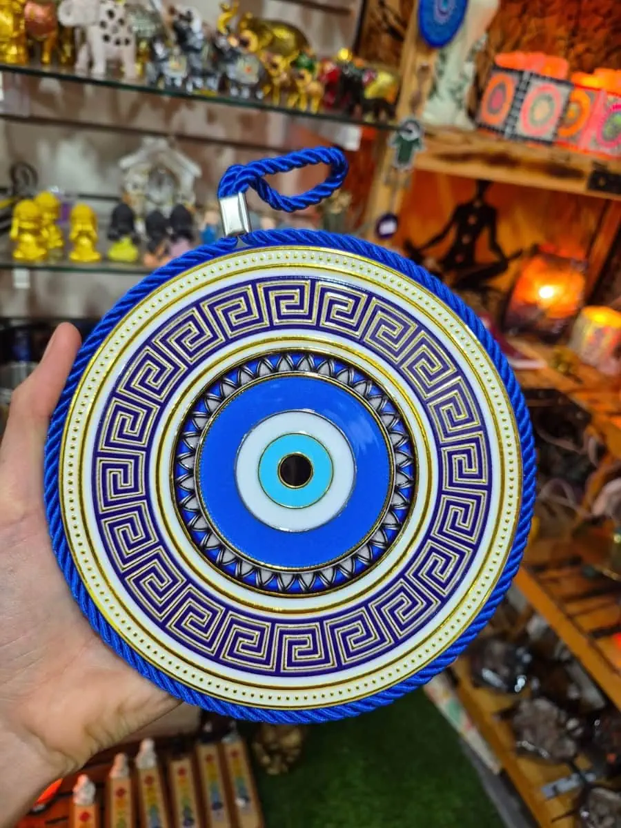 Colgante de ojo turco redondo azul y celeste con guarda griega azul oscuro, fondo blanco, detalles dorados y cordón azul