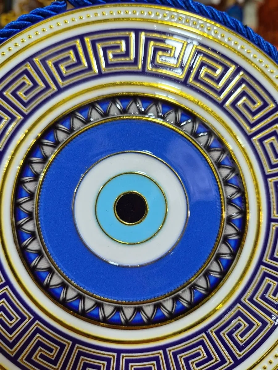 Colgante de ojo turco redondo azul y celeste con guarda griega azul oscuro, fondo blanco, detalles dorados y cordón azul
