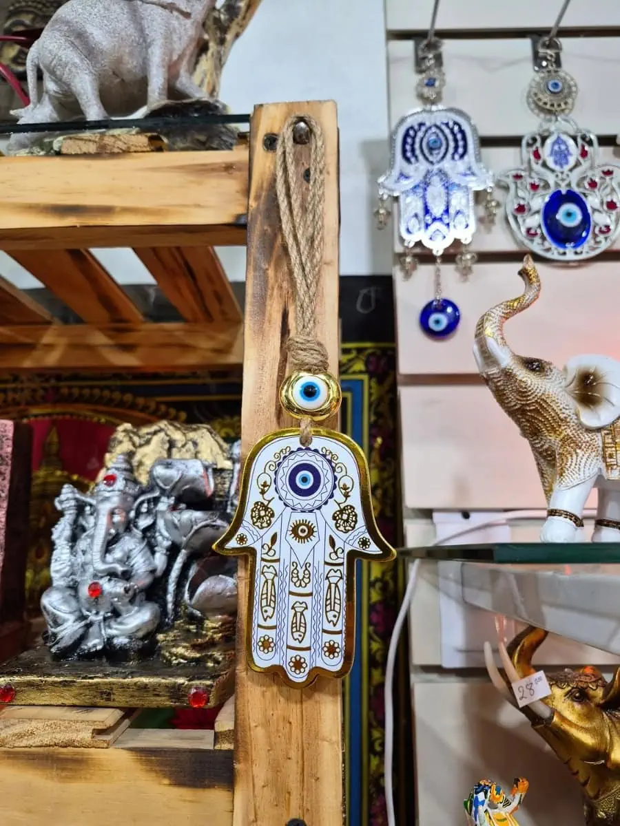 Mano de Fátima blanca con dibujos dorados, ojo turco azul central y detalle de ojo protector sobre cordón de soga