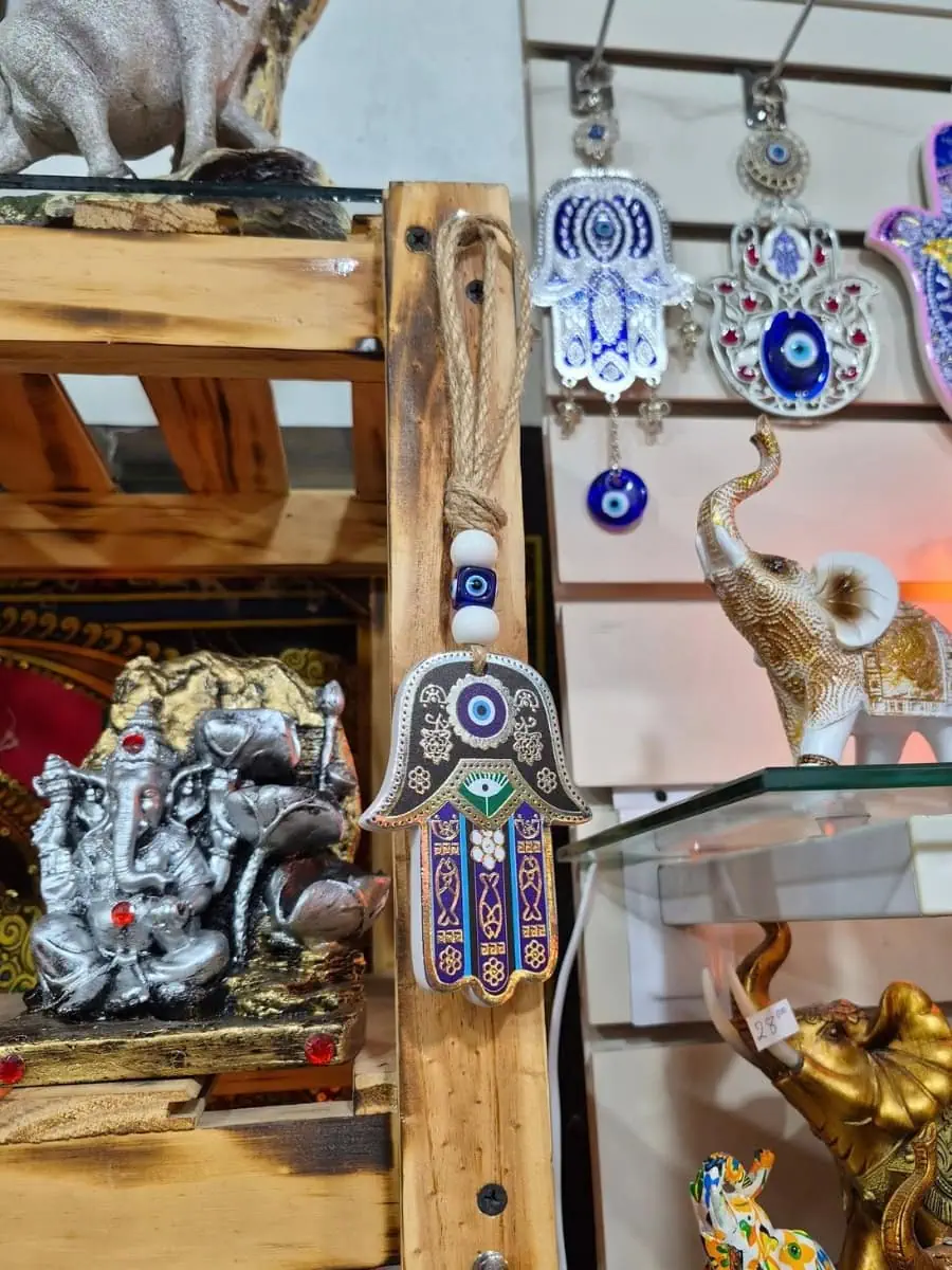 Colgante Mano de Fátima con bordes plateados, detalles azules y violetas, ojo turco y cuentas blancas sobre cordón