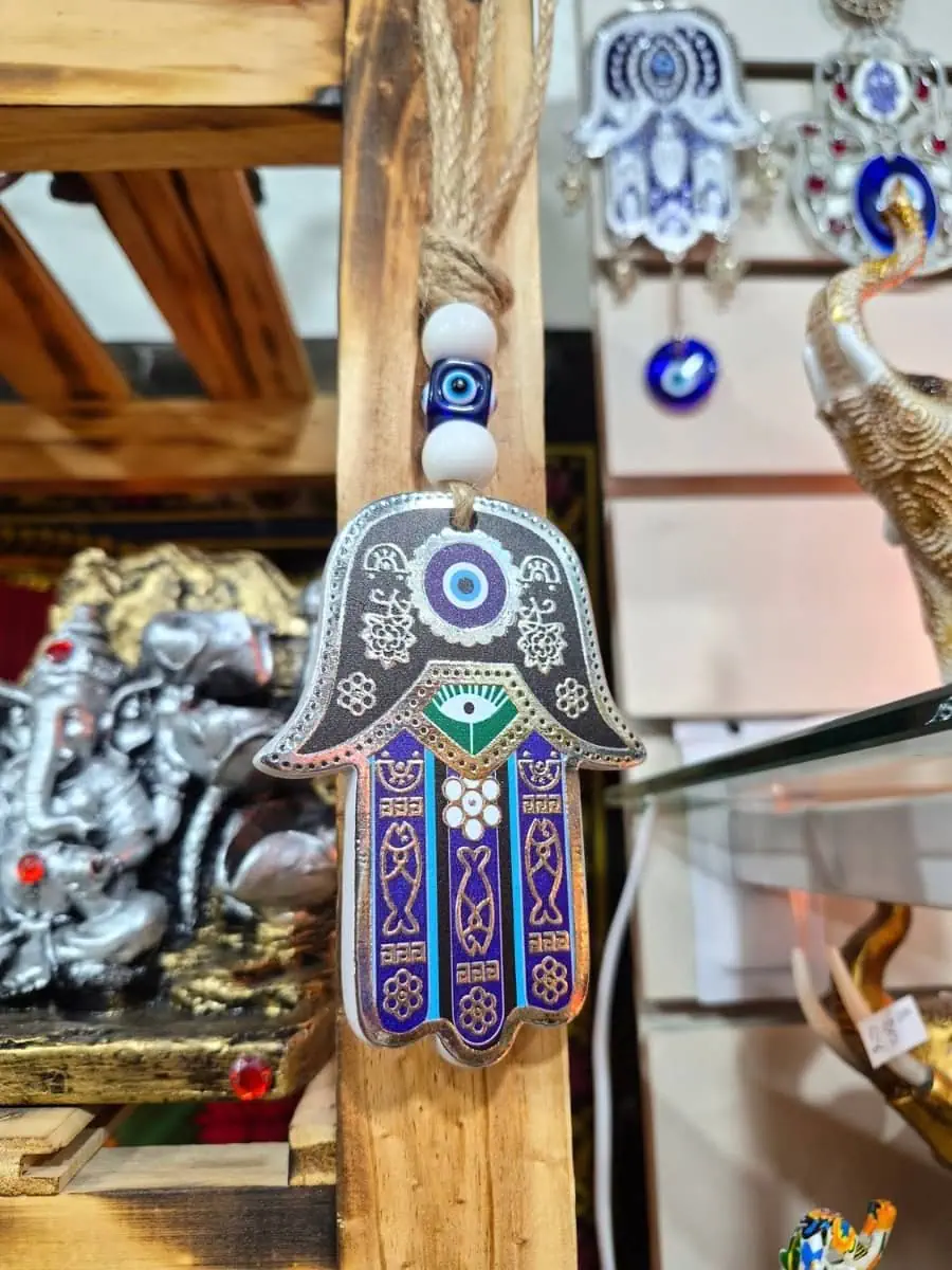 Colgante Mano de Fátima con bordes plateados, detalles azules y violetas, ojo turco y cuentas blancas sobre cordón