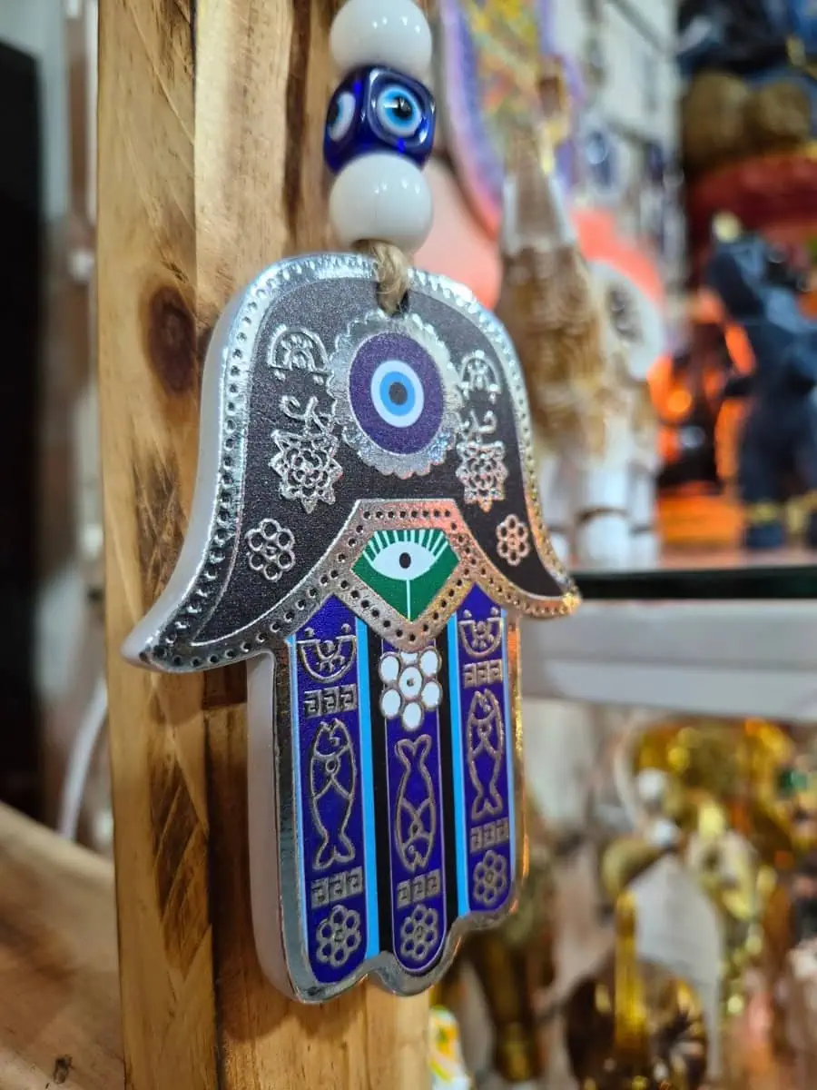 Colgante Mano de Fátima con bordes plateados, detalles azules y violetas, ojo turco y cuentas blancas sobre cordón