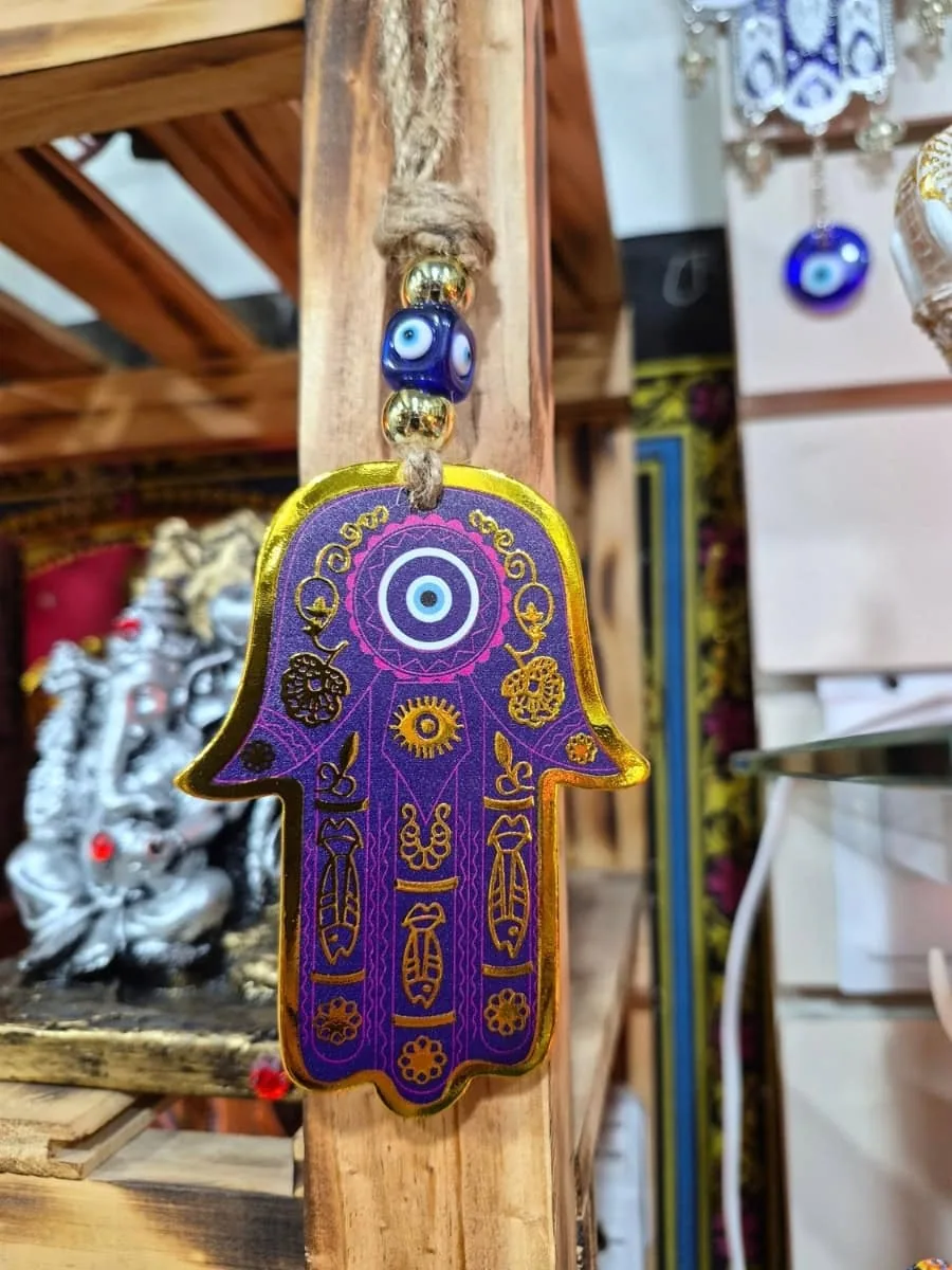 Mano de Fátima violeta con bordes dorados, ojo turco azul y dibujos ornamentales sobre cordón de soga
