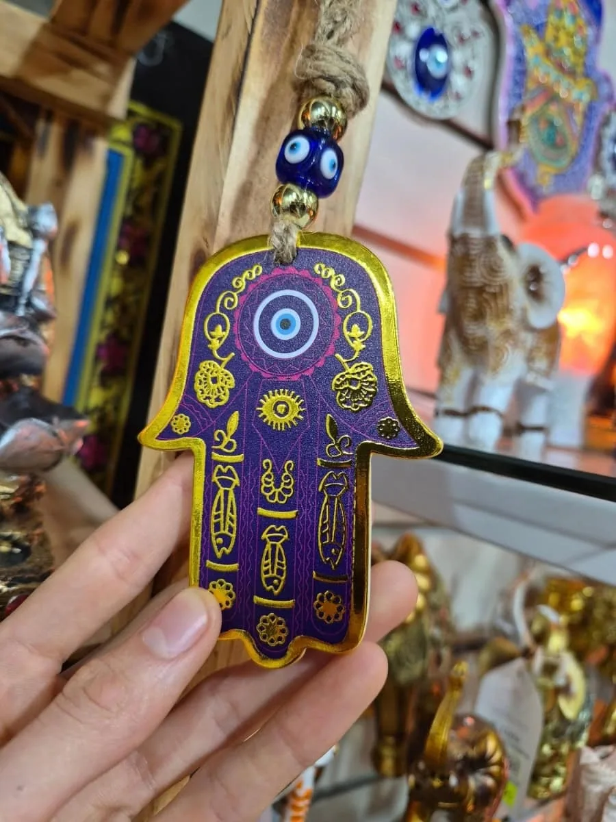 Mano de Fátima violeta con bordes dorados, ojo turco azul y dibujos ornamentales sobre cordón de soga