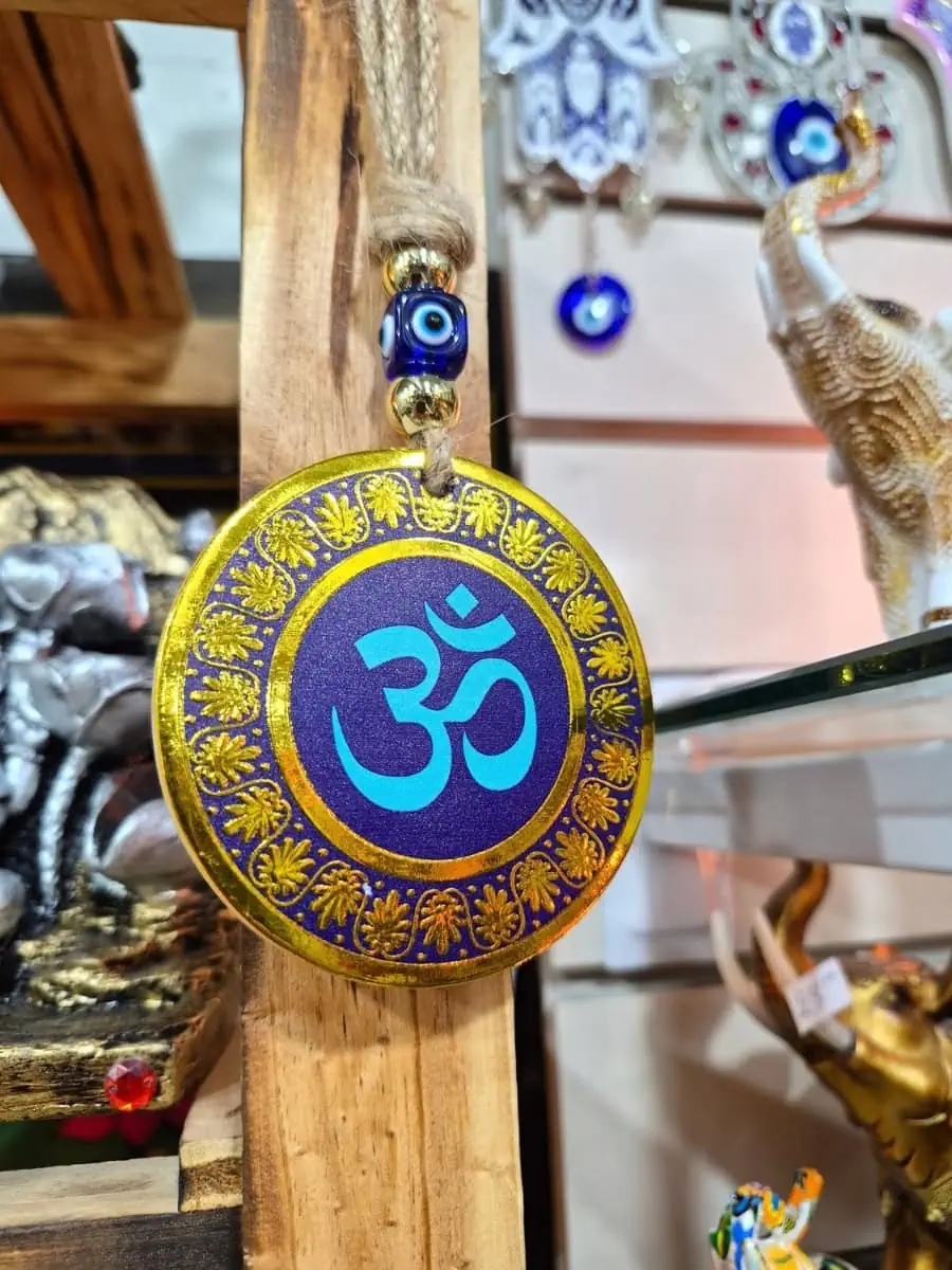 Colgante circular violeta con símbolo Om celeste, borde de flores doradas y cuenta de ojo turco azul