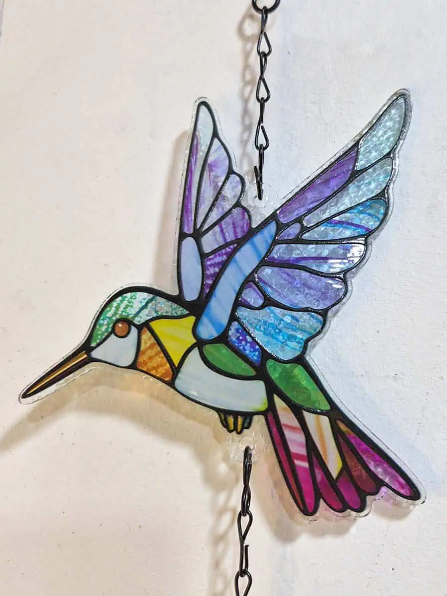 Colgante decorativo de colibrí en vitró celeste, lila, verde y rosa con campana de metal