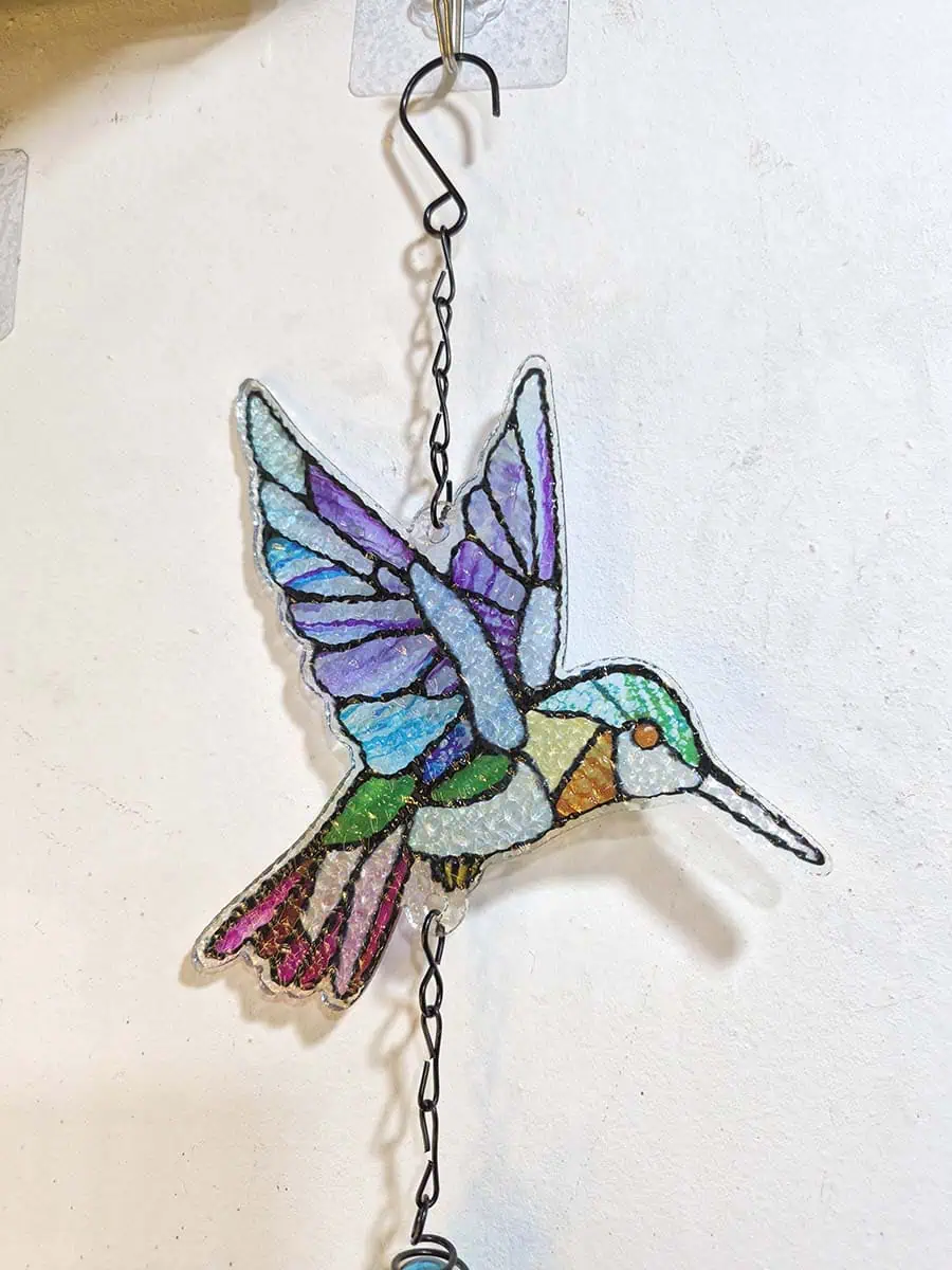 Colgante decorativo de colibrí en vitró celeste, lila, verde y rosa con campana de metal