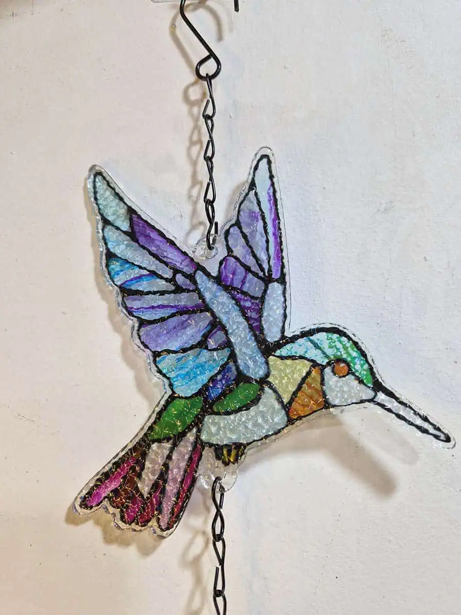 Colgante decorativo de colibrí en vitró celeste, lila, verde y rosa con campana de metal