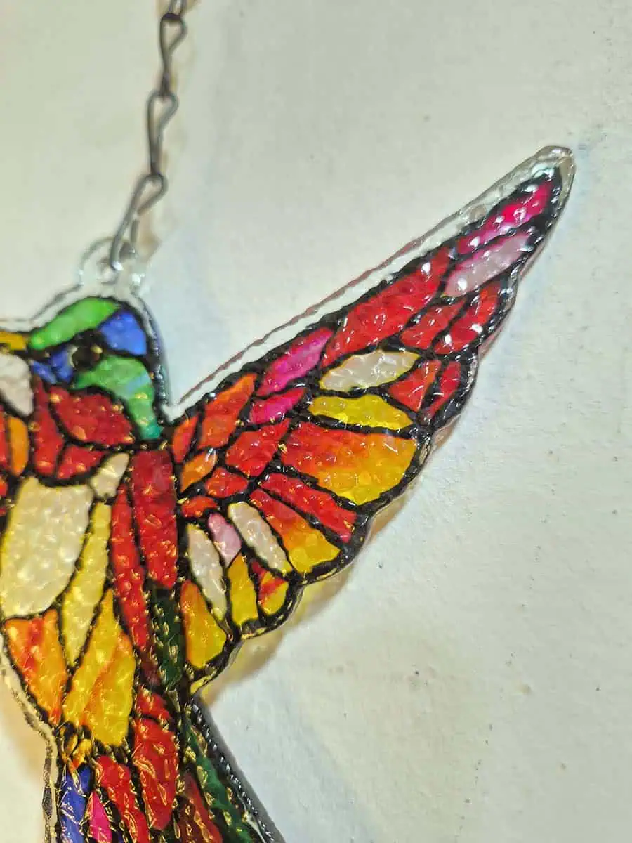Colgante decorativo de colibrí en vitró rojo y rosa con detalles amarillos y campana de metal