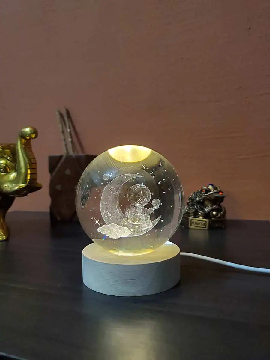Lámpara esfera de cristal con diseño 3D de un Astronauta sentado en la luna con eschufe USB