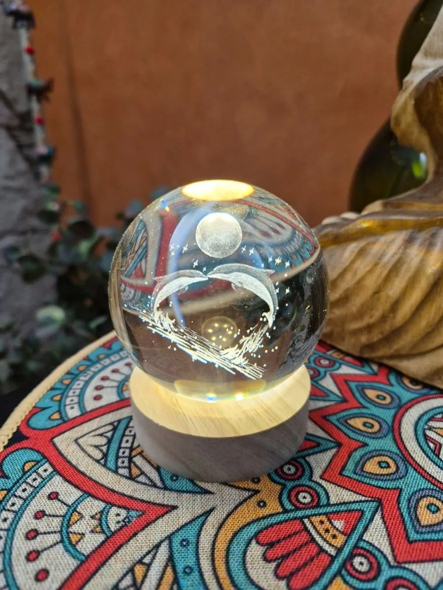 Lámpara esfera de cristal 3D con dos delfines bajo la luna, iluminada con luz cálida sobre base de madera