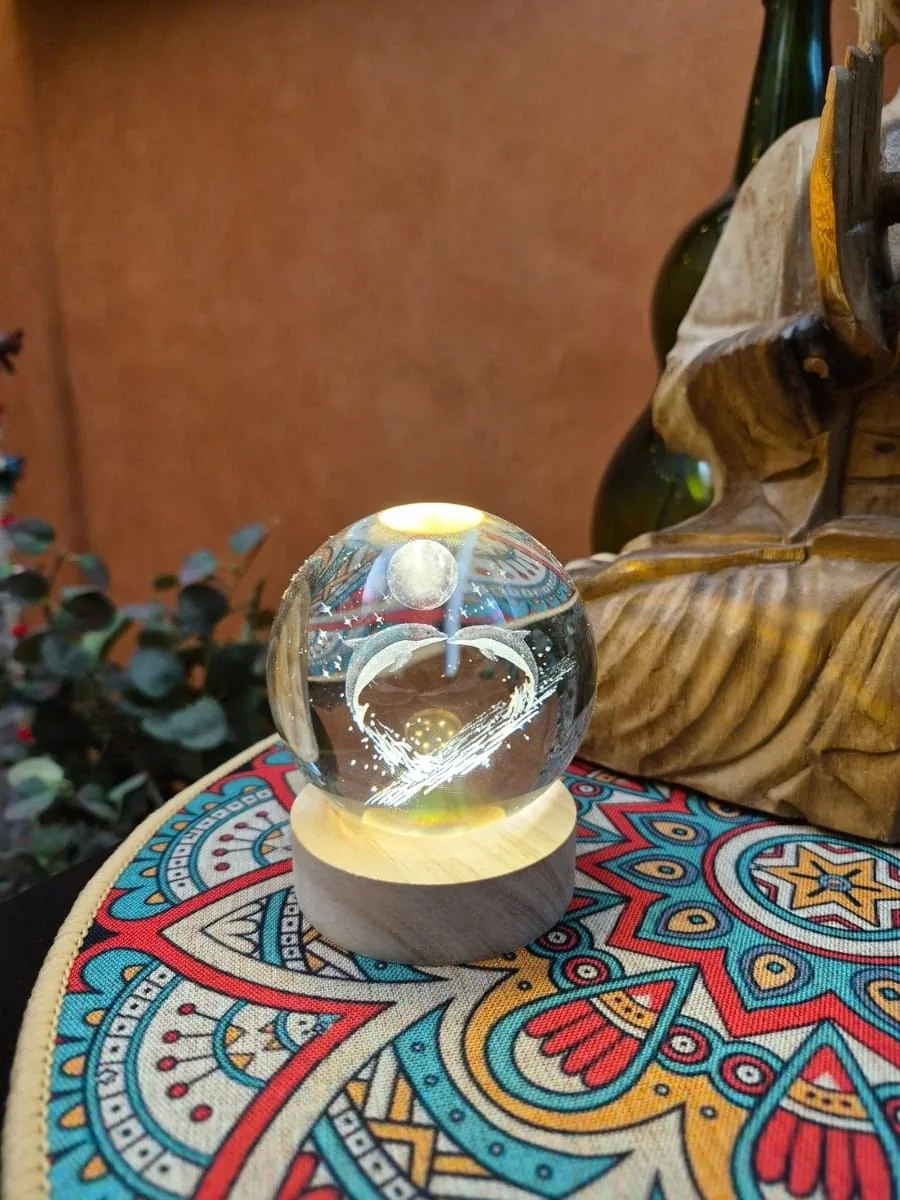 Lámpara esfera de cristal 3D con dos delfines bajo la luna, iluminada con luz cálida sobre base de madera