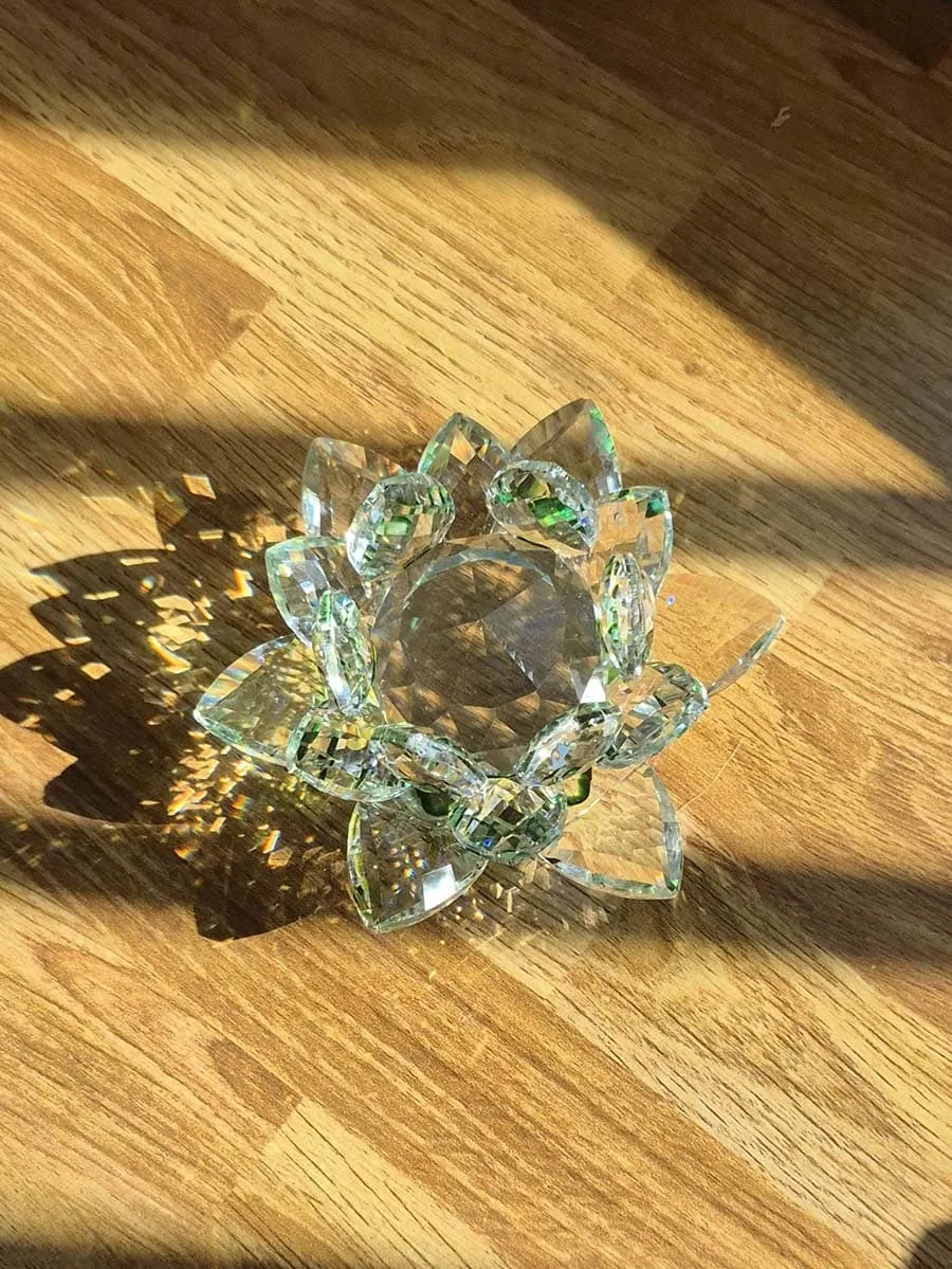 Flor de loto grande de vidrio transparente con detalles verdes, varias capas de pétalos facetados y reflejos de luz solar