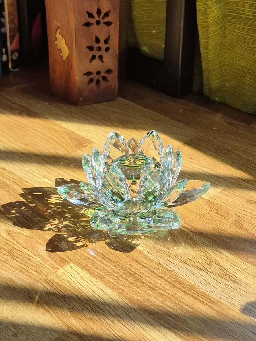 Flor de loto grande de vidrio transparente con detalles verdes, varias capas de pétalos facetados y reflejos de luz solar