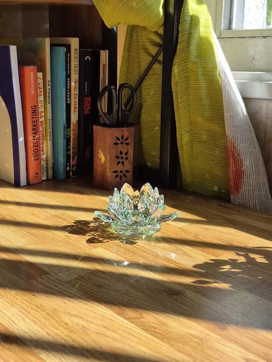 Flor de loto grande de vidrio transparente con detalles verdes, varias capas de pétalos facetados y reflejos de luz solar