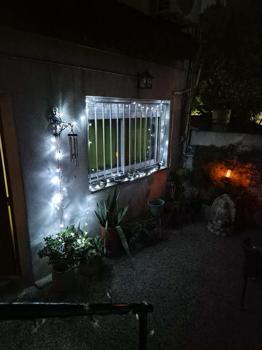 Guirnalda solar de flores blancas de 10 metros iluminando plantas y una ventana en un jardín.