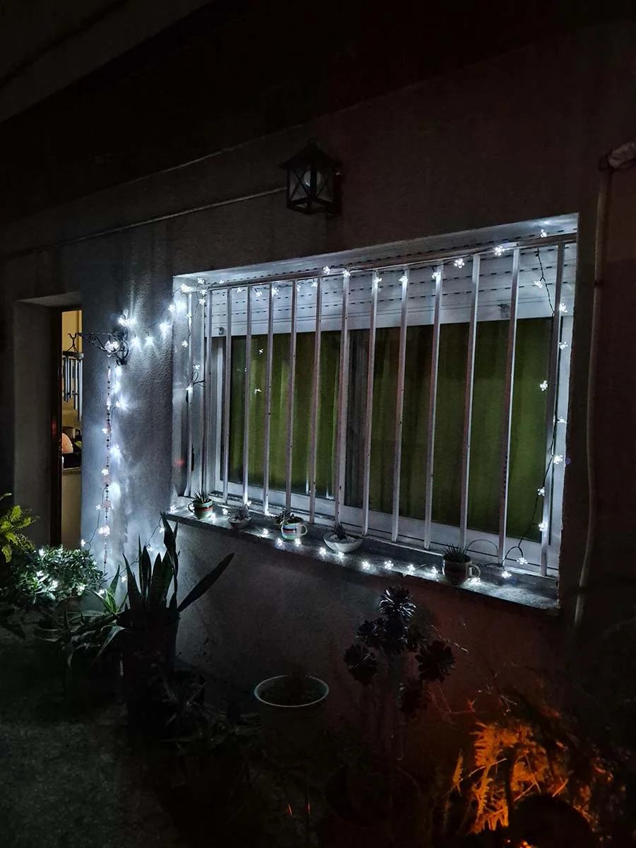 Guirnalda solar de flores blancas de 10 metros iluminando plantas y una ventana en un jardín.