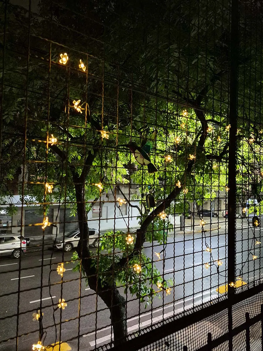 Guirnalda solar de flores con luz cálida de 10 metros decorando la reja de un balcón durante la noche.