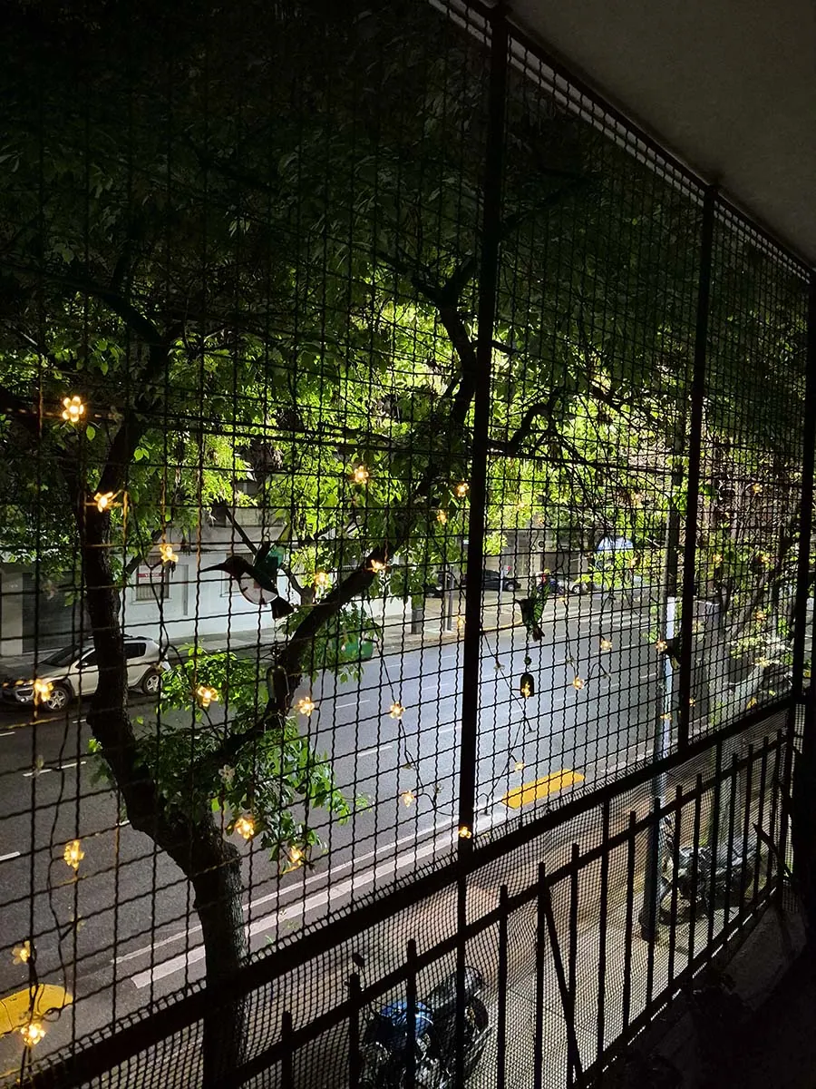 Guirnalda solar de flores con luz cálida de 10 metros decorando la reja de un balcón durante la noche.