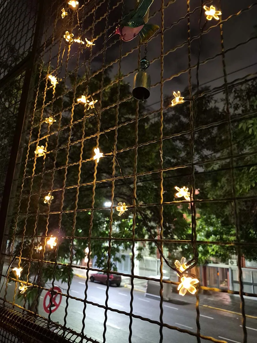 Guirnalda solar de flores con luz cálida de 10 metros decorando la reja de un balcón durante la noche.