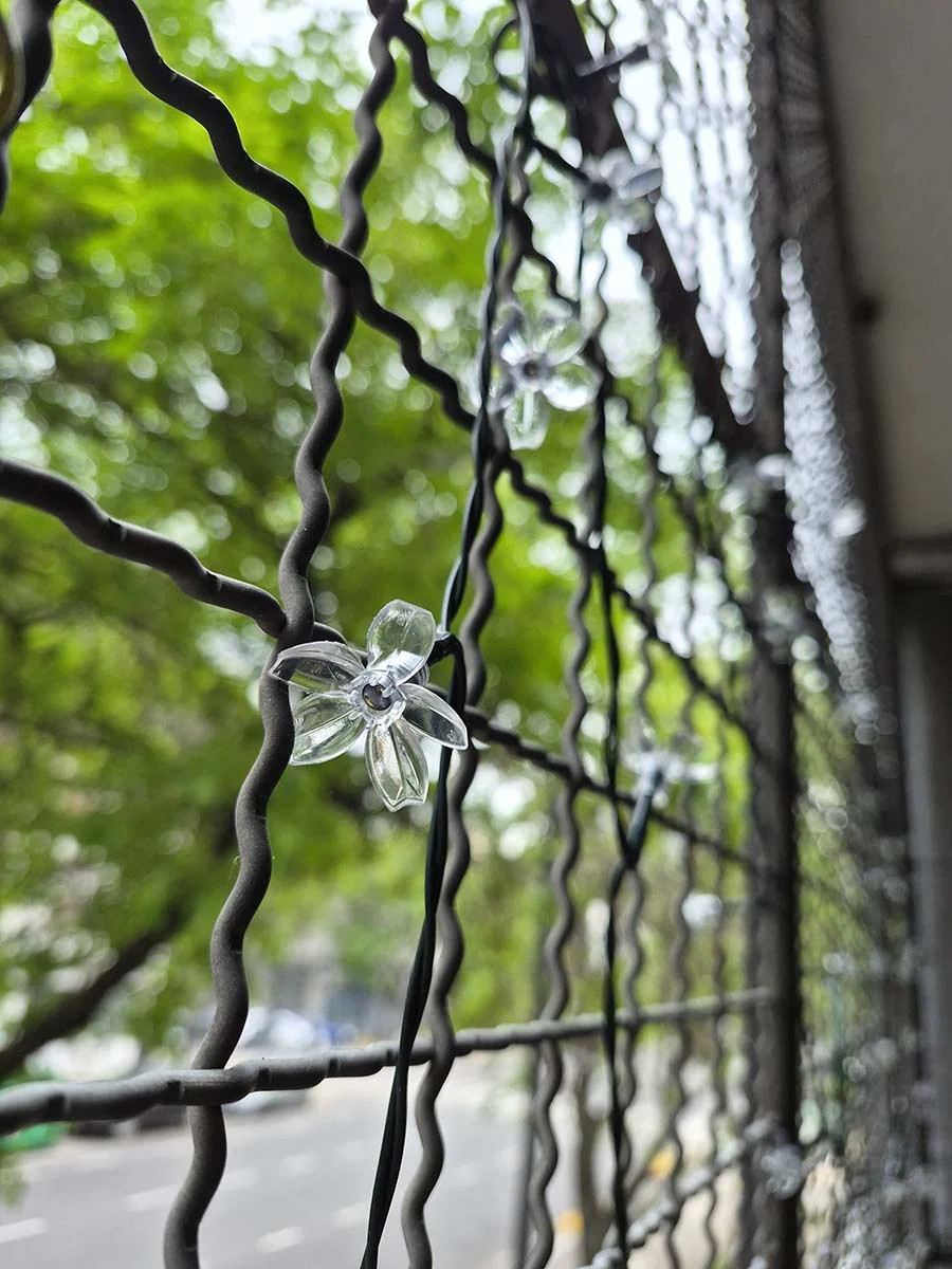 Guirnalda solar de flores con luz cálida de 10 metros decorando la reja de un balcón durante la noche.