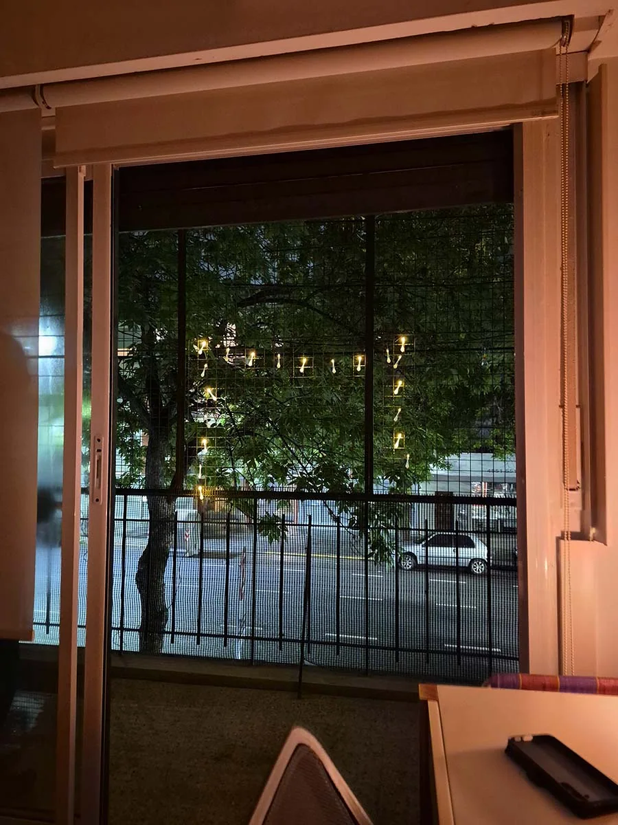 Guirnalda solar de gotas transparentes con luz cálida de 5 metros decorando la reja de un departamento.