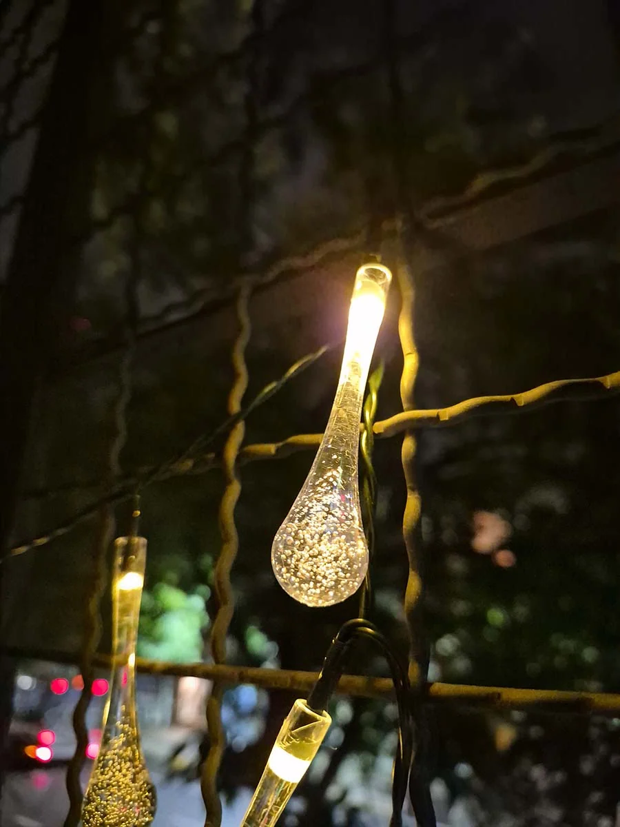 Guirnalda solar de gotas transparentes con luz cálida de 5 metros decorando la reja de un departamento.