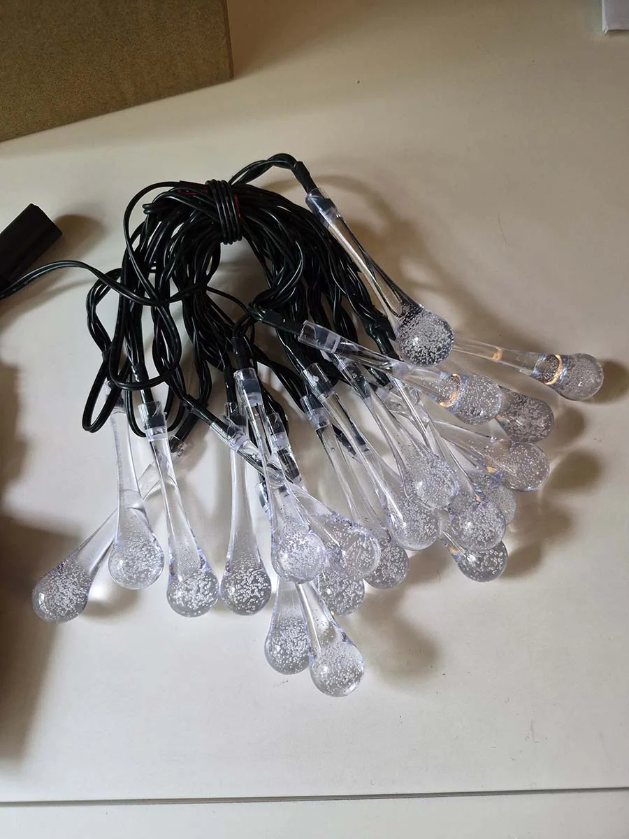 Guirnalda solar de gotas transparentes con luz cálida de 5 metros decorando la reja de un departamento.