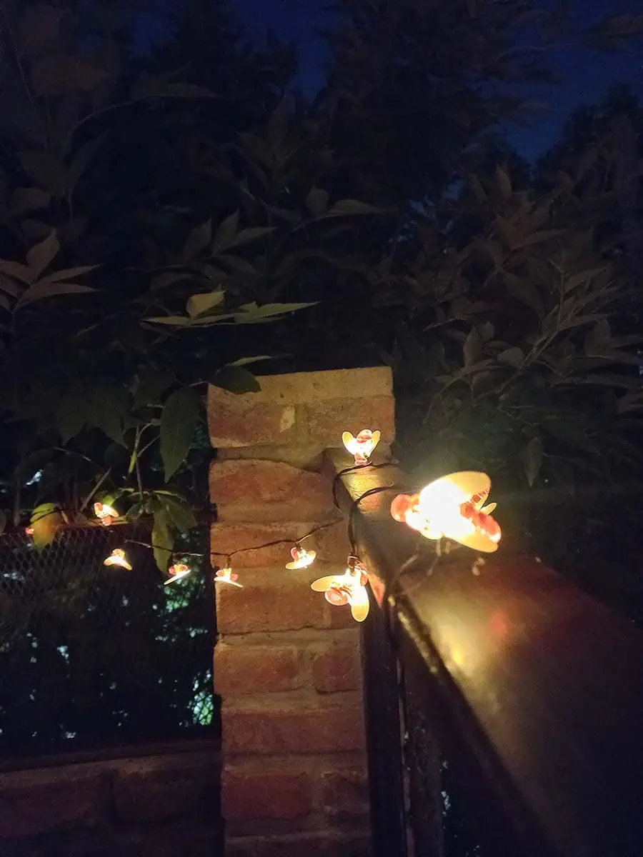 Guirnalda solar de abejitas con luz cálida decorando la baranda y pared de una terraza durante la noche.