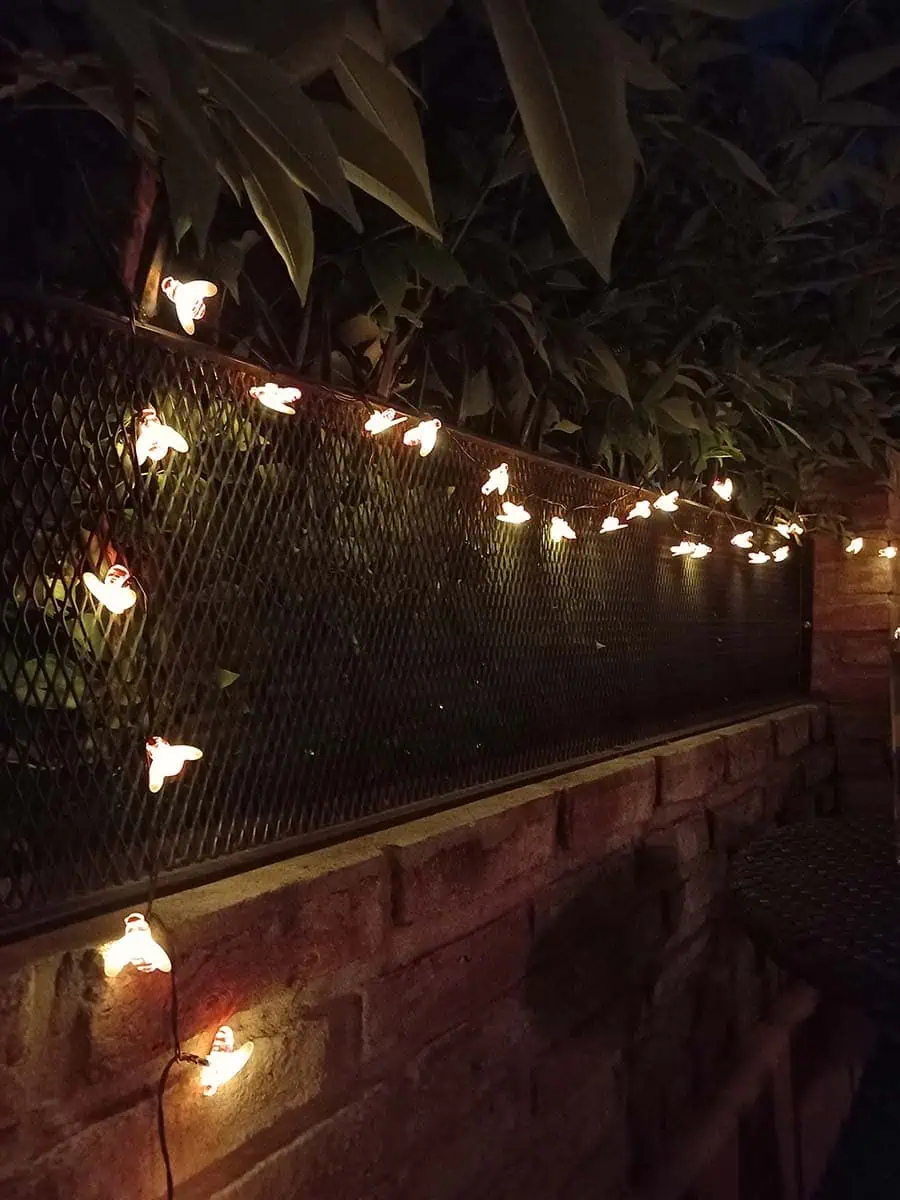 Guirnalda solar de abejitas con luz cálida decorando la baranda y pared de una terraza durante la noche.