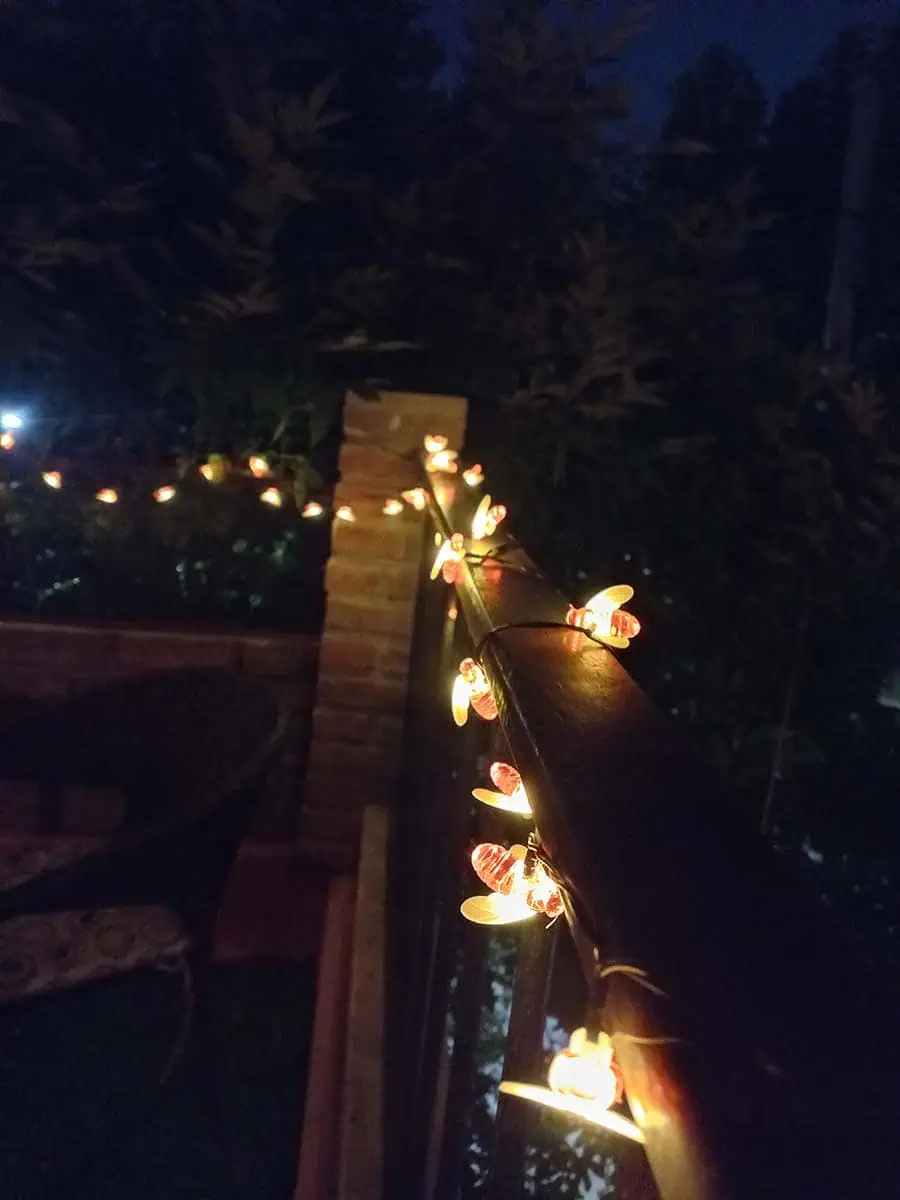 Guirnalda solar de abejitas con luz cálida decorando la baranda y pared de una terraza durante la noche.