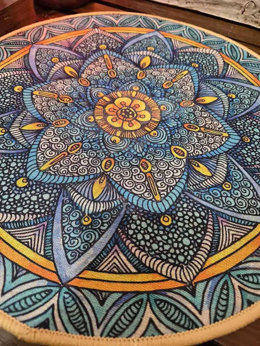 Individual redondo con mandala gris, celeste y naranja con diseño floral detallado